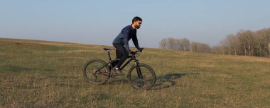 Şortlu ve formalı bisikletçi, modern karbon kuyruklu motorsikletli. Uçurumun kenarında, yeşil bahar ormanlarının arka planında duran bir hava süspansiyon çatalı var.