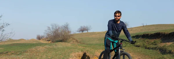 Cyclist in shorts and jersey on a modern carbon hardtail bike with an air suspension fork standing on a cliff against the background of fresh green spring forest