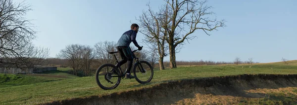 Cyclist in shorts and jersey on a modern carbon hardtail bike with an air suspension fork standing on a cliff against the background of fresh green spring forest