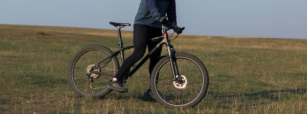 Cyclist in shorts and jersey on a modern carbon hardtail bike with an air suspension fork standing on a cliff against the background of fresh green spring forest