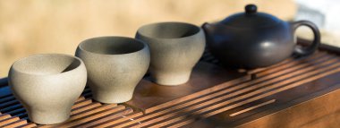 Çin çay seremonisi. Balçıktan yapılmış seramik çaydanlık ve ahşap bir arka planda kaseler.