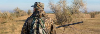 Avlanırken vahşi kuşları ya da av hayvanlarını arayan kamuflajlı silahlı bir avcı..