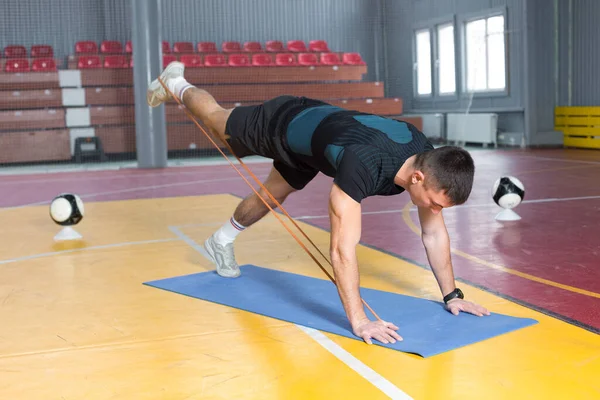 Athletic guy in sportswear and fitness tracker doing exercises in gym.