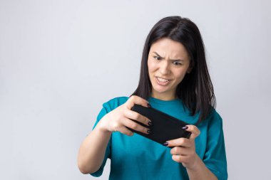 Gri arka planda cep telefonu kullanan gülümseyen genç kadının ön portresi