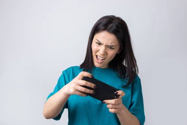 Gri arka planda cep telefonu kullanan gülümseyen genç kadının ön portresi