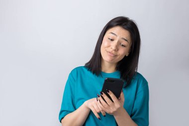 Gri arka planda cep telefonu kullanan gülümseyen genç kadının ön portresi