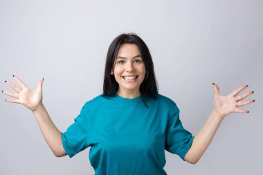 Gri arka planda duran şaşırmış yüz ifadesiyle genç ve güzel bir kadın..