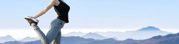 A thin athletic girl takes a break between classes on the background of mountains in the early morning, enjoys silence and freedom.