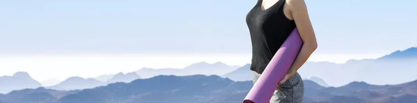 A thin athletic girl takes a break between classes on the background of mountains in the early morning, enjoys silence and freedom.