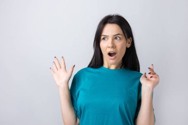 Gri arka planda duran şaşırmış yüz ifadesiyle genç ve güzel bir kadın..