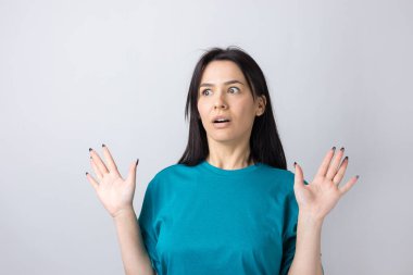 Gri arka planda duran şaşırmış yüz ifadesiyle genç ve güzel bir kadın..