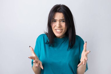 Gri arka planda duran şaşırmış yüz ifadesiyle genç ve güzel bir kadın..