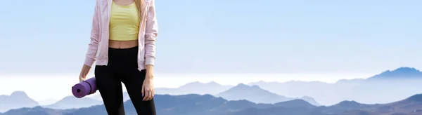 A thin athletic girl takes a break between classes on the background of mountains in the early morning, enjoys silence and freedom.