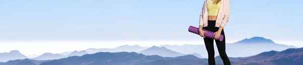 A thin athletic girl takes a break between classes on the background of mountains in the early morning, enjoys silence and freedom.