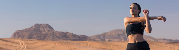 A thin athletic girl takes a break between classes on the background of mountains in the early morning