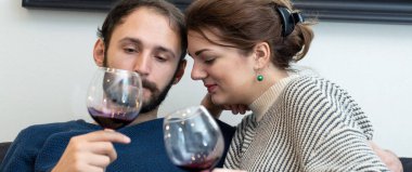 Genç ve mutlu bir çift şarap içip evde dinleniyor.