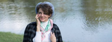 Parktaki genç kadın cep telefonuyla konuşuyor. Fransız tarzında şirin bir kız portresi..