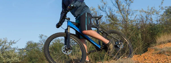 Conquering mountain peaks by cyclist in shorts and jersey on a modern carbon hardtail bike with an air suspension fork .