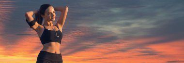 Tozlu, spor ayakkabılı ve üstü açık bir kız antrenman minderiyle egzersiz aralarında dinleniyor. Güzel atmosferik dramatik bulutlar.