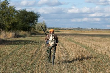 Kamuflaj kıyafeti giymiş silahlı bir avcı. Silahlı bir beyefendi, orta ölçekli, tanınmaz halde..