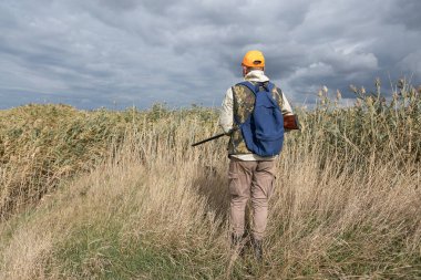 Kamuflaj kıyafeti giymiş silahlı bir avcı. Silahlı bir beyefendi, orta ölçekli, tanınmaz halde..