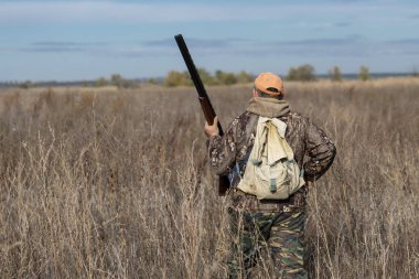 Kamuflaj kıyafeti giymiş silahlı bir avcı. Silahlı bir beyefendi, orta ölçekli, tanınmaz halde..