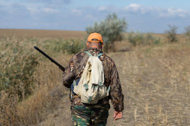 Kamuflaj kıyafeti giymiş silahlı bir avcı. Silahlı bir beyefendi, orta ölçekli, tanınmaz halde..