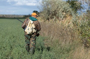 Kamuflaj kıyafeti giymiş silahlı bir avcı. Silahlı bir beyefendi, orta ölçekli, tanınmaz halde..