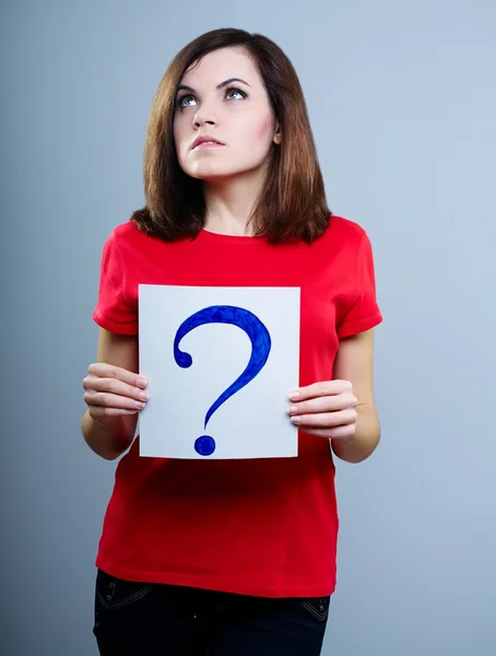 Thoughtful girl in a red T-shirt on a gray background holding a question mark — Stock Photo, Image