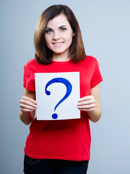 Thoughtful girl in a red T-shirt on a gray background holding a question mark — Stock Photo, Image