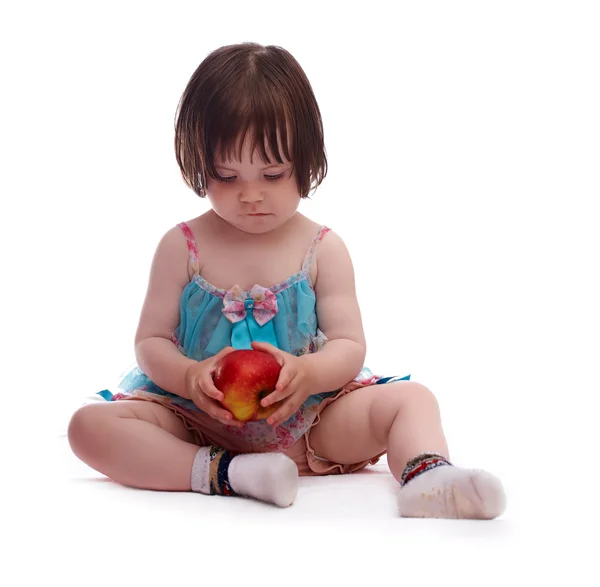 Baby girl in a colorful dress playing with red apple Stock Photo by