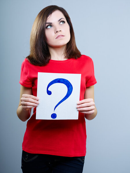 thoughtful girl in a red T-shirt on a gray background holding a question mark