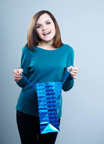 Fată zâmbitoare într-un tricou albastru care deține un sac de cumpărături .Pe un fundal gri — Fotografie, imagine de stoc