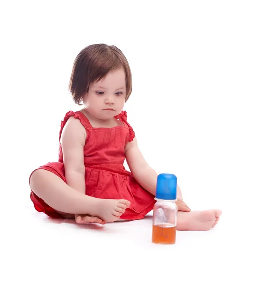 Bebé niña en vestido rojo aislado sobre fondo blanco mirando una botella de jugo —  Fotos de Stock