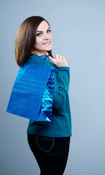 Menina sorridente em uma camiseta azul segurando um saco de compras. Em um fundo cinza — Fotografia de Stock
