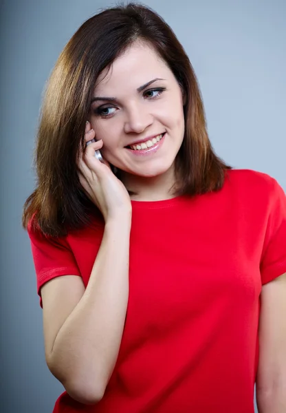 Beautiful girl in a red T-shirt and jeans holding a folder and looking at it on a gray background — Stock Photo, Image