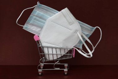 Bir FFP2 maskesi ve bir alışveriş arabasında kahverengi bir arka planda cerrahi ağız koruyucusu.