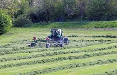 Bavyera 'da bir çiftçi samanı kesiyor. Bir traktör tarlada samanı döndürür.