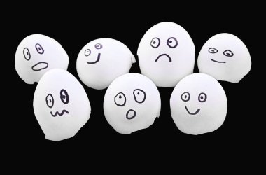 Üzerinde yüzler olan yumurta kabukları farklı duyguları gösteriyor, siyah bir arkaplanda izole edilmiş.