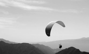 Bir paraglider planörüyle Alpler 'in üzerinde yüzüyor. Bir paraglider 'ın siyah beyaz fotoğrafı.