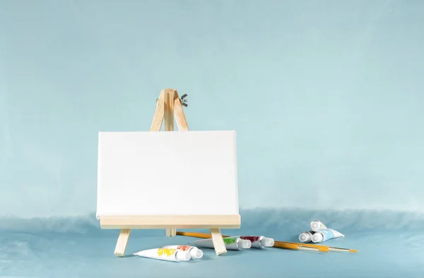 Pequeno cavalete com uma tela em branco em um fundo azul com água — Fotografia de Stock