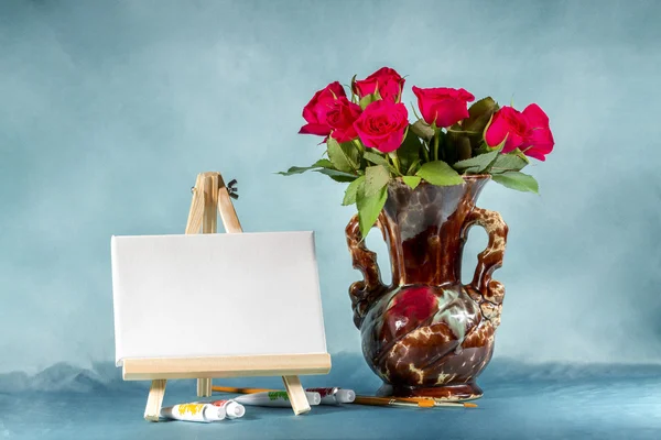 Natureza morta com um buquê de rosas, cavalete e tintas . — Fotografia de Stock