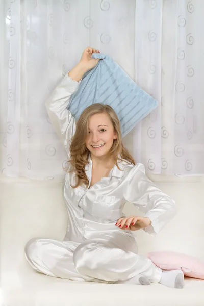 Young woman in pajamas sitting and holding pillow — Stock Photo, Image