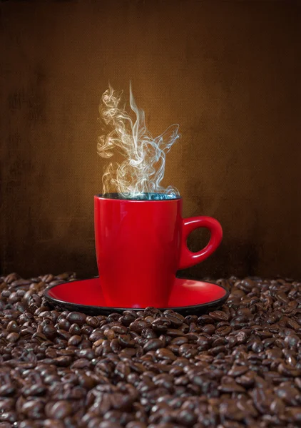 Red cup of coffee with steam on a background of coffee beans. — Stock Photo, Image