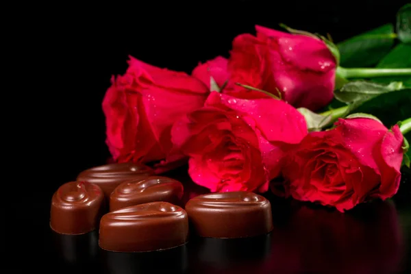 Chocolate candies with a bouquet of roses on a black background — Stock Photo, Image
