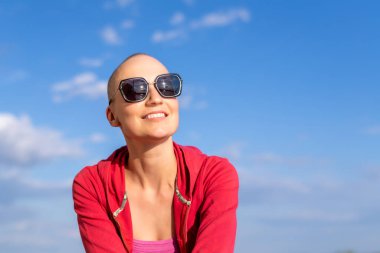 Genç, güzel, mutlu, çekici, beyaz, kel, güneş gözlüklü kadın portresi. Uzaklara bakmayı ve açık havada mavi gökyüzüne gülümsemeyi seviyor. Kendinden emin, neşeli kadın.