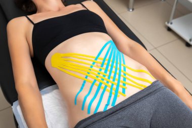 Yukarıda, koltukta uzanan genç, ince, sportif bayanın karın kaslarına mavi yapışkan elastik tedavi bandı yapıştırırken yatıyordu. Yaralı rehabilitasyon ve sağlık hizmetleri