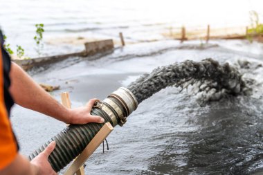 Güç pompası makinesinin enerji borusu yere kum kumu ile çamur atığı suyu döküyor. Kum temizleme ve kıyı kesme. Septik kanalizasyon bakım servisi. Endüstriyel çevre kirliliği.