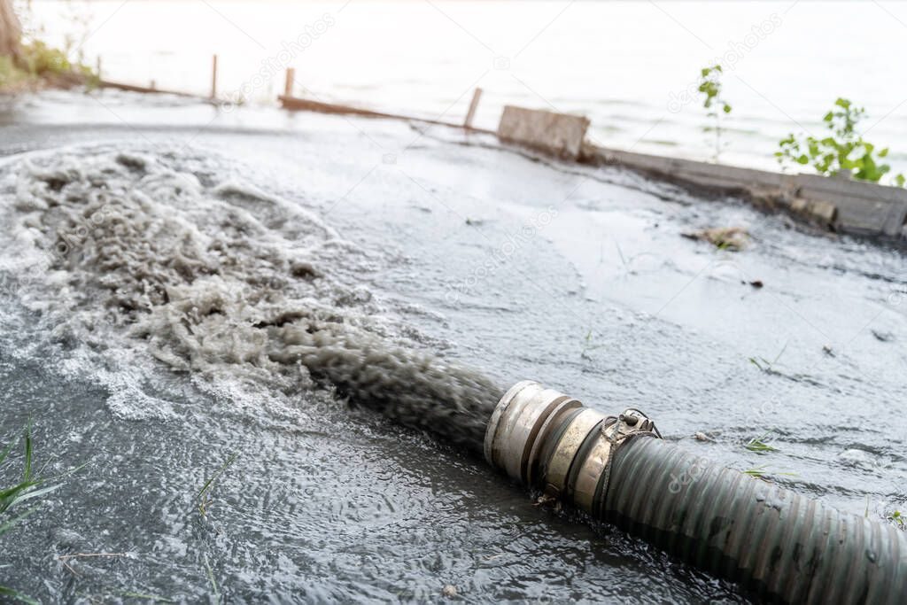 Close-up big pipe of power pump machine pouring mud sludge waste water with sand and silt on ground. Sand-wash and coast-depeening. Septic sewage maintenance service. Industrial environment pollution