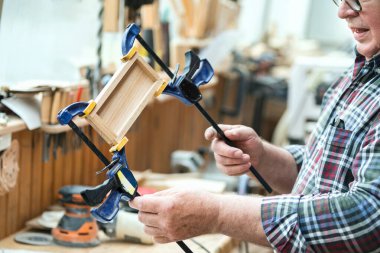 Kıdemli marangoz ahşap kaplama yüzeyi yapıştırıyor ve kıskaçlara katılıyor. Atölyede ekipman ve aletlerle marangoz. El yapımı döşeme. Ahşap parçası yapıştırıcı.